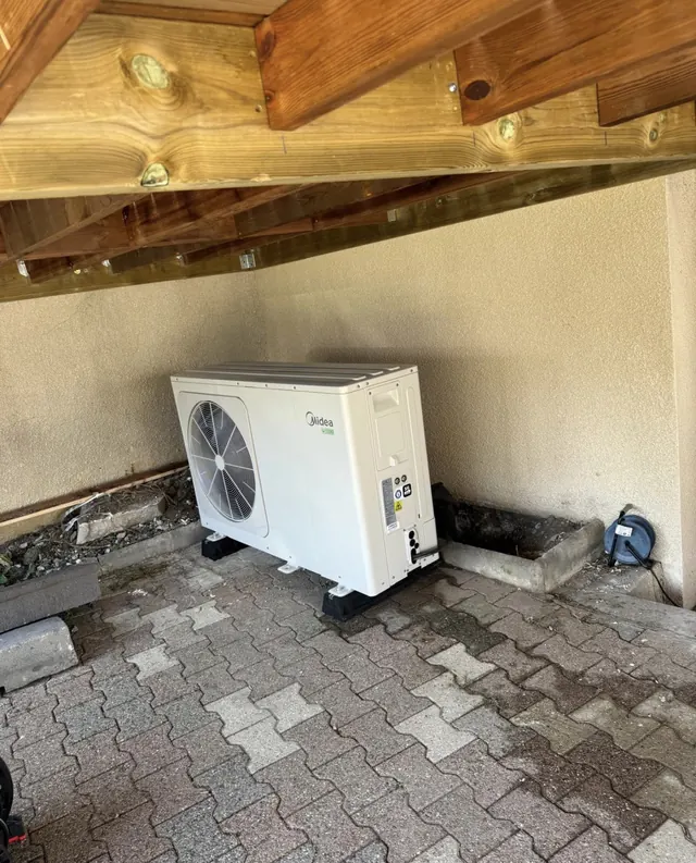 Unité extérieure Midea installée sur supports sous un auvent en bois