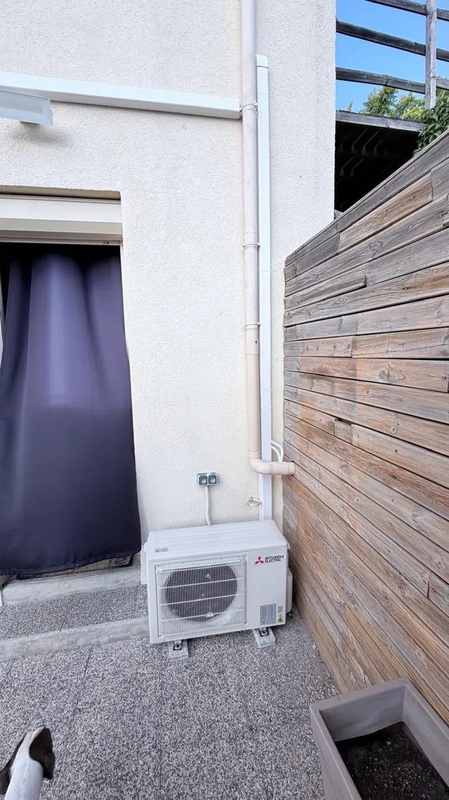 Unité extérieure Mitsubishi Electric posée au sol le long d’un bardage bois, liaisons sous goulotte en façade