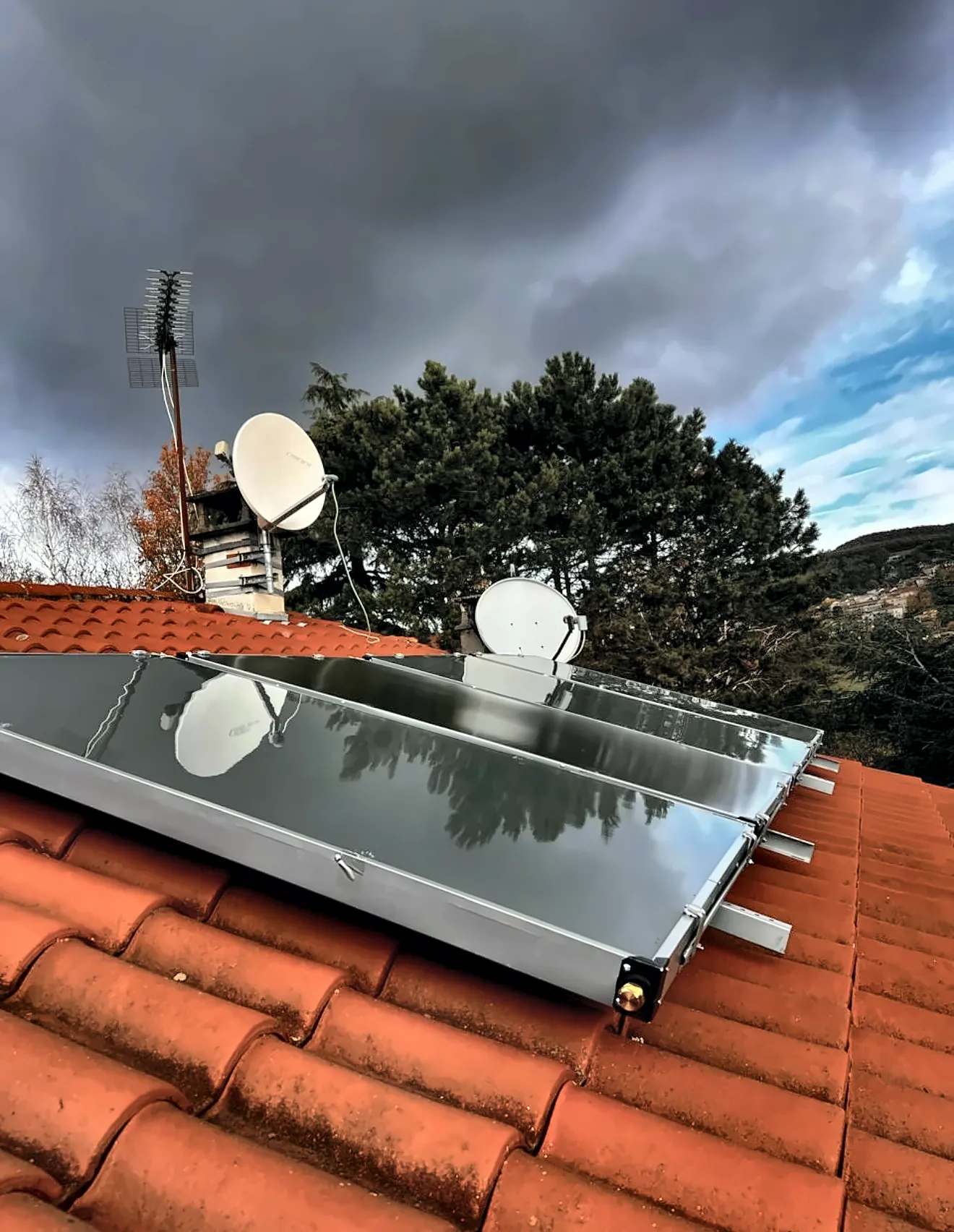 Capteurs solaires thermiques posés sur une toiture en tuiles, sous un ciel d’orage